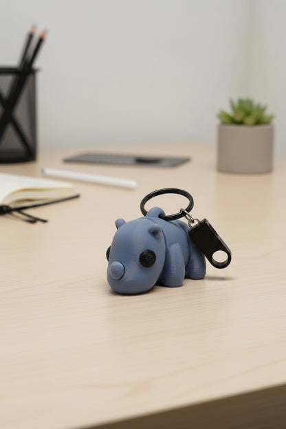 Blue grey baby rhino shaped keychain on a desk with office supplies in the background